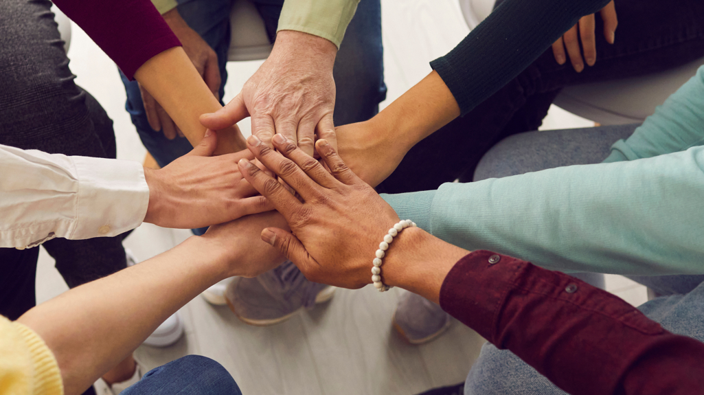 Seven people's hands all on top of each other in the middle to represent a team