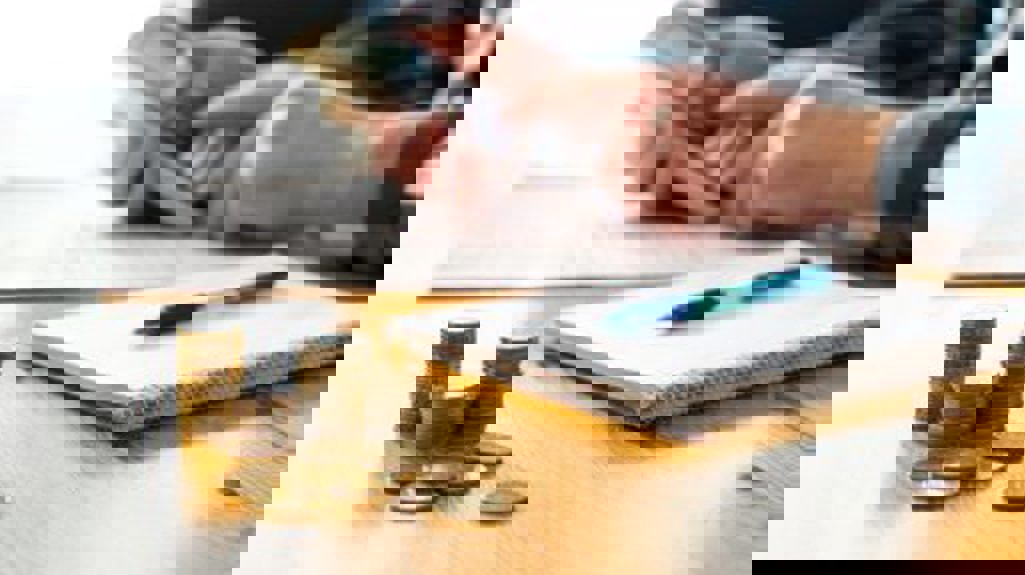 Desk With Money, Pen And Notepad, And Person Using Calculator