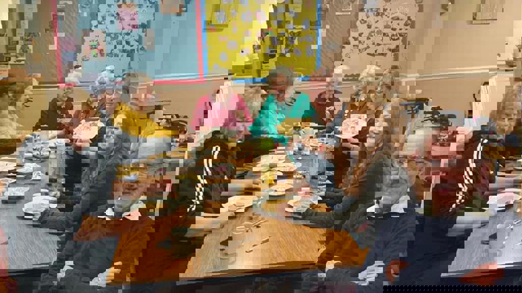 Group of people sitting round a table smiling and holding plates of pancakes