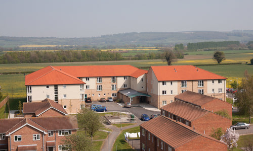 A photograph of a few different houses and a building of flats with fields in the background and a grey sky.