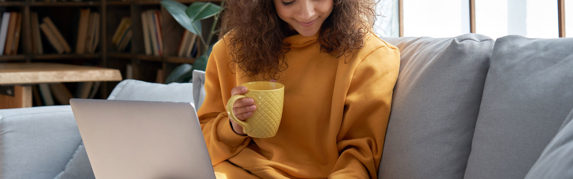 Women sitting on the sofa in a yellow jumper, stroking a cat with a laptop on her knee