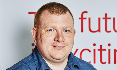 A picture of a man in a denim shirt smiling at the camera.