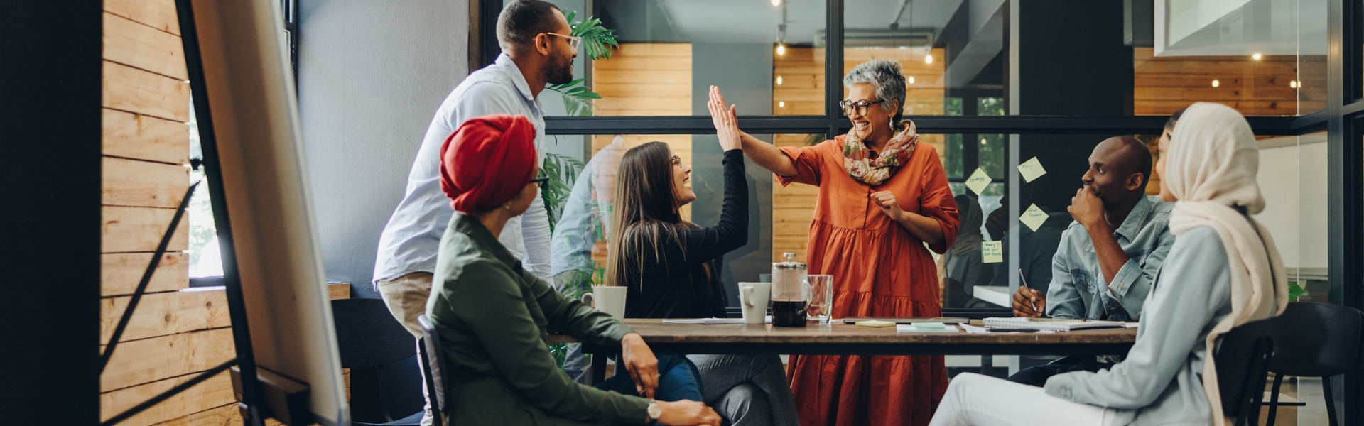 A group of colleagues celebrating with two women high fiving in the middle, in an office environment. 
