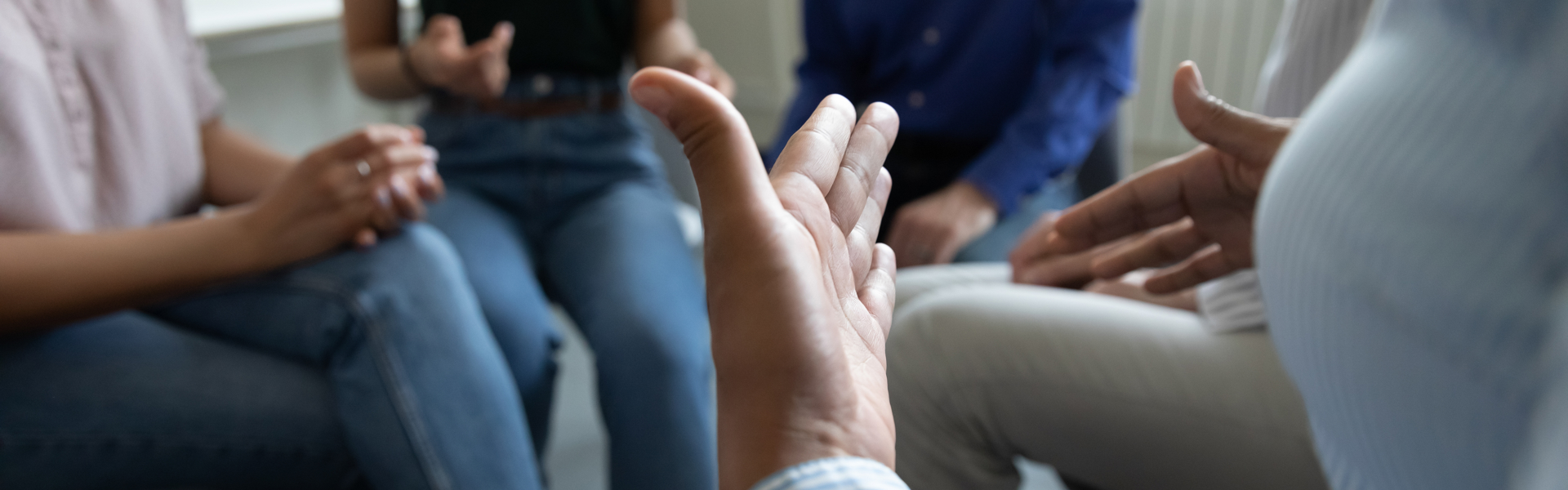Abstract picture of people sat in a circle with one person gesturing using their hands