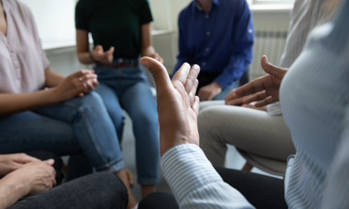 Abstract picture of people sat in a circle with one person gesturing using their hands