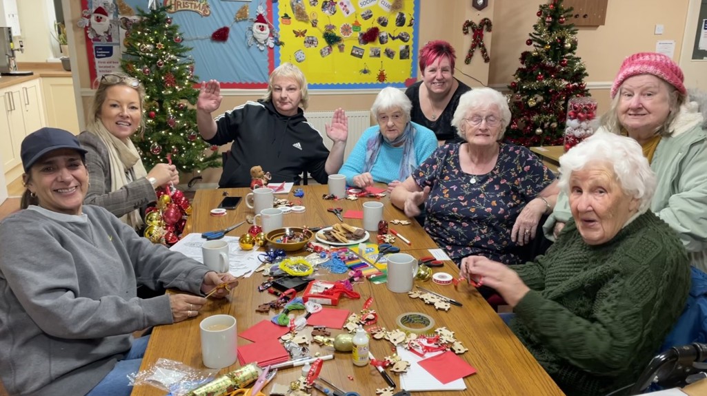 A photograph of some Christmas crafts taking place with people smiling around a table. 