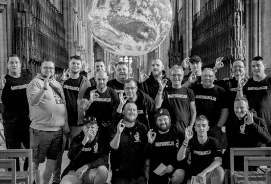An Andy's Man Club meeting with everyone doing a 'okay' sign with their hands which is the Andy's Man Club symbol 