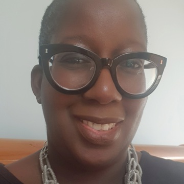 Sarah's headshot - Sarah's smiling at the camera and wearing black chunky glasses and a silver necklace with a black top