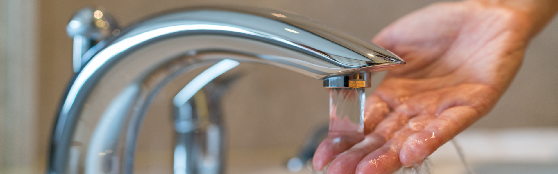 Tap running with a hand testing the temperature of the water