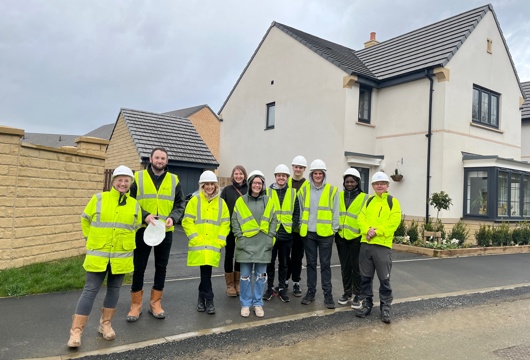 A group of students standing infront of a new build development all wearing high visibility clothing 