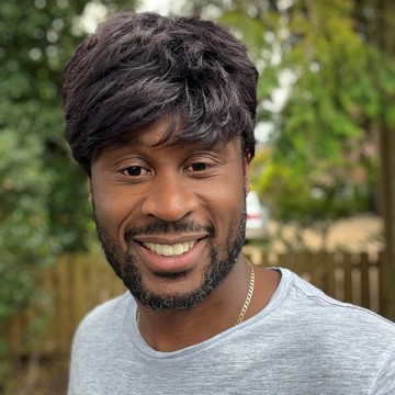 Man wearing grey top smiling at the camera, he's in a leafy garden 