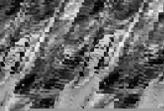 A black and white image of Leanne stood smiling at the camera with woodland behind