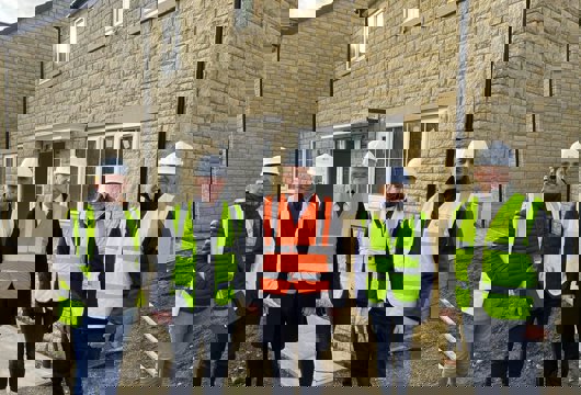 Group of four men and one woman wearing hi-vis jackets and hard hats standing outside a new house